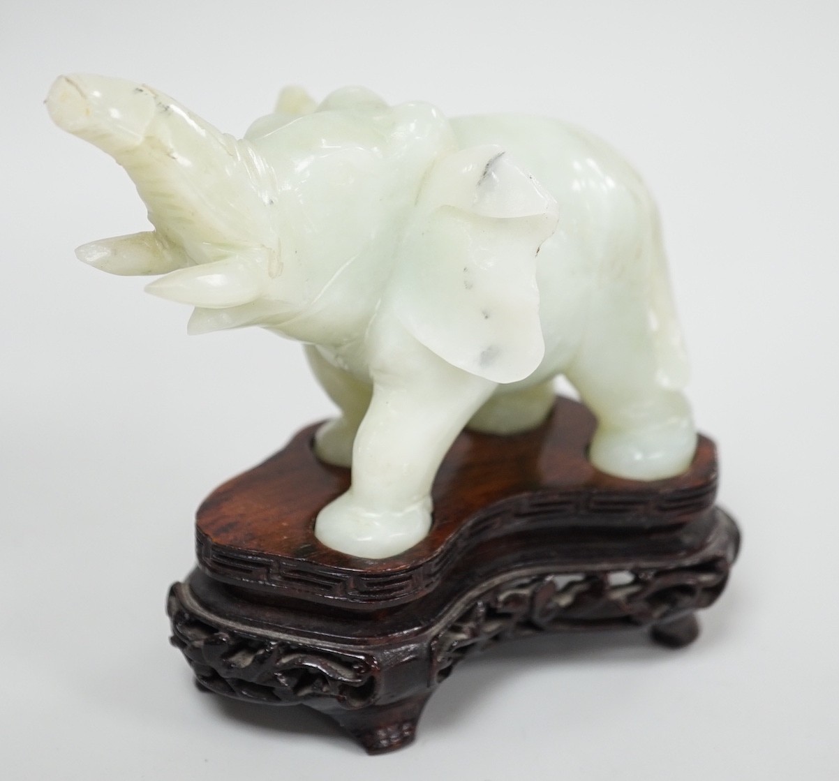 A Chinese bowenite jade elephant on hard wood stand, 11cm tall